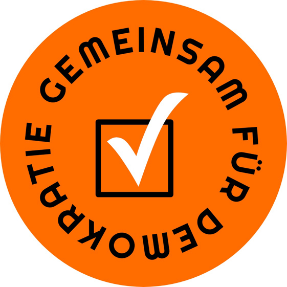 Gemeinsam für Demokratie. Logo vor orangefarbenem Grund. Die Schrift ist im Kreis gesetzt. In der Mitte dominiert ein Check-Haken.